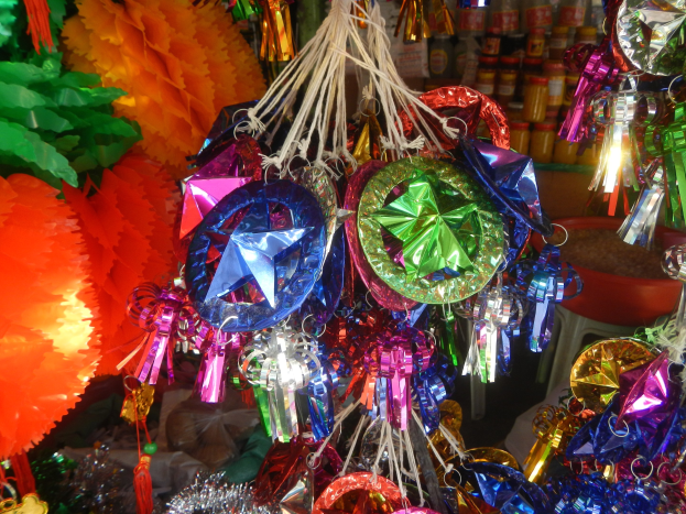Farbenfrohe Festschmuck-Dekorationen, darunter Laternen und Bänder, hängen von der Decke über Regalen mit Flaschen im Hintergrund.